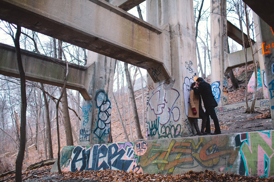 Couple kissing by a bridge with graffiti
